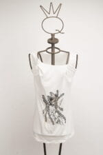 Top bianco con dettagli grafici neri, presentato su un manichino con testa a forma di corona. Ideale per un look casual e alla moda.