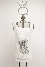 Top bianco con dettagli grafici neri, presentato su un manichino con testa a forma di corona. Ideale per un look casual e alla moda.