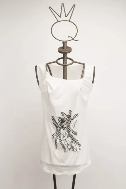 Top bianco con dettagli grafici neri, presentato su un manichino con testa a forma di corona. Ideale per un look casual e alla moda.