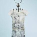 Abito femminile con maniche corte, caratterizzato da un design artistico in bianco e nero su fondo chiaro. Indossato su un manichino con un supporto a forma di corona, il vestito presenta dettagli grafici e un taglio asimmetrico, ideale per look casual e creativi. Sfondo azzurro che mette in risalto il capo.