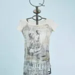 Abito femminile con maniche corte, caratterizzato da un design artistico in bianco e nero su fondo chiaro. Indossato su un manichino con un supporto a forma di corona, il vestito presenta dettagli grafici e un taglio asimmetrico, ideale per look casual e creativi. Sfondo azzurro che mette in risalto il capo.