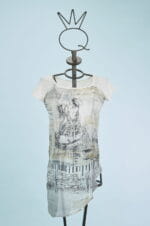 Abito femminile con maniche corte, caratterizzato da un design artistico in bianco e nero su fondo chiaro. Indossato su un manichino con un supporto a forma di corona, il vestito presenta dettagli grafici e un taglio asimmetrico, ideale per look casual e creativi. Sfondo azzurro che mette in risalto il capo.