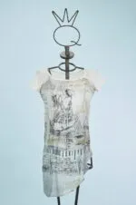 Abito femminile con maniche corte, caratterizzato da un design artistico in bianco e nero su fondo chiaro. Indossato su un manichino con un supporto a forma di corona, il vestito presenta dettagli grafici e un taglio asimmetrico, ideale per look casual e creativi. Sfondo azzurro che mette in risalto il capo.