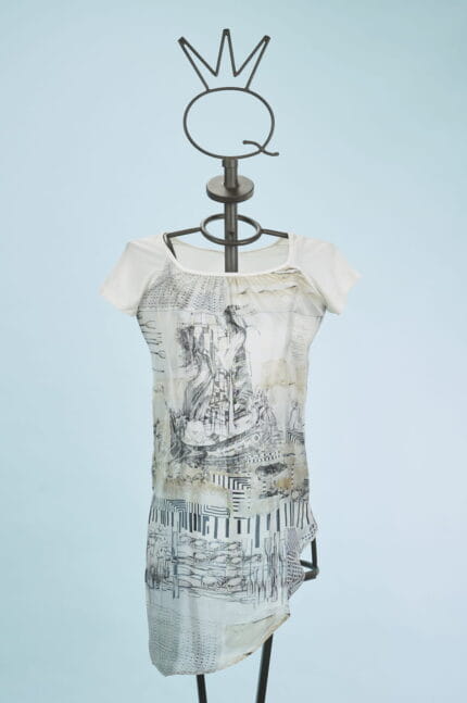 Abito femminile con maniche corte, caratterizzato da un design artistico in bianco e nero su fondo chiaro. Indossato su un manichino con un supporto a forma di corona, il vestito presenta dettagli grafici e un taglio asimmetrico, ideale per look casual e creativi. Sfondo azzurro che mette in risalto il capo.