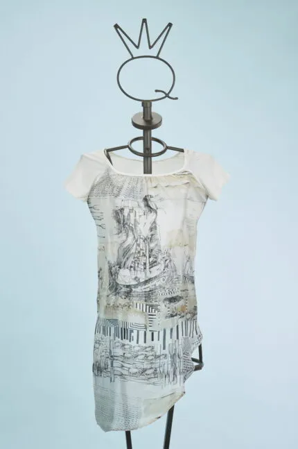 Abito femminile con maniche corte, caratterizzato da un design artistico in bianco e nero su fondo chiaro. Indossato su un manichino con un supporto a forma di corona, il vestito presenta dettagli grafici e un taglio asimmetrico, ideale per look casual e creativi. Sfondo azzurro che mette in risalto il capo.