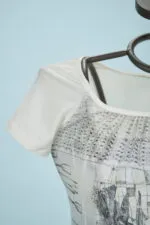 T-shirt bianca con maniche corte e design grafico, in esposizione su un manichino, su sfondo azzurro. Perfetta per un look estivo casual e alla moda.