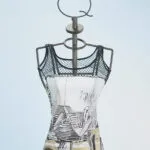 Top in tessuto con stampa artistica su manichino, caratterizzato da spalline in rete nera e design moderno. Sfondo azzurro chiaro.