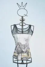 Top in tessuto con stampa artistica su manichino, caratterizzato da spalline in rete nera e design moderno. Sfondo azzurro chiaro.