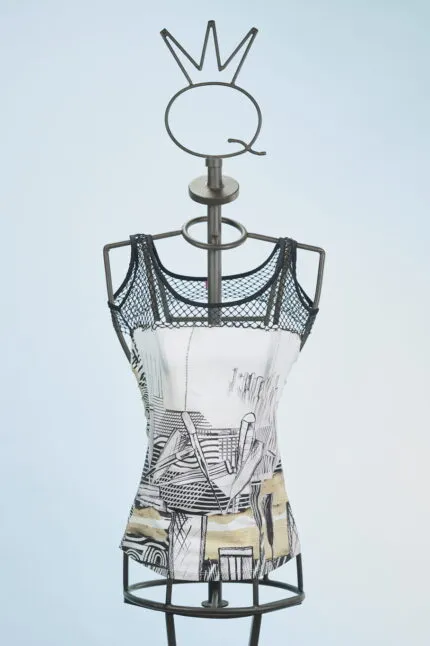 Top in tessuto con stampa artistica su manichino, caratterizzato da spalline in rete nera e design moderno. Sfondo azzurro chiaro.