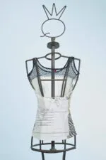 Top femminile su manichino, caratterizzato da una rete nera e dettagli grafici su sfondo bianco, ideale per un look estivo casual.