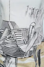Dettaglio di una maglietta con un design artistico che presenta linee nere su sfondo chiaro, raffigurante strumenti da disegno e trame geometriche.