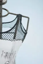 Top di moda con rete nera su manichino, dettagli artistici e sfondo blu chiaro. Perfetto per collezioni di abbigliamento contemporaneo e creativo.