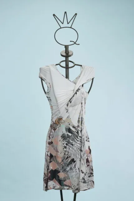 Abito estivo elegante in tessuto leggero, presentato su un manichino con supporto artistico. Il vestito presenta un design innovativo con dettagli floreali e geometrici, ideale per occasioni casual e formali. Sfondo azzurro che mette in risalto il capo.