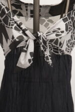 Abito elegante con scollo a V e nodo centrale, caratterizzato da un design grafico in bianco e nero. La parte superiore è in tessuto leggero, mentre la gonna è di un materiale scuro e fluttuante, ideale per occasioni estive.