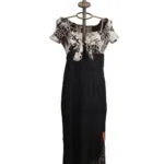 Abito lungo da donna con maniche corte e scollatura a V, caratterizzato da un top in bianco e nero con motivo floreale e una gonna nera con ricami colorati. Esposto su un manichino con una base decorativa.