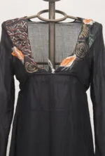 Abito nero con ricami floreali colorati, maniche lunghe e scollatura a V, esposto su un manichino. Ideale per occasioni eleganti o casual.