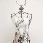 Manichino con top bianco decorato da un design artistico in bianco e nero, esposto su uno sfondo neutro. Il top presenta dettagli grafici colorati e un'originale scollatura asimmetrica, ideale per la moda contemporanea.