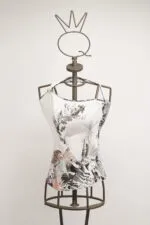 Manichino con top bianco decorato da un design artistico in bianco e nero, esposto su uno sfondo neutro. Il top presenta dettagli grafici colorati e un'originale scollatura asimmetrica, ideale per la moda contemporanea.