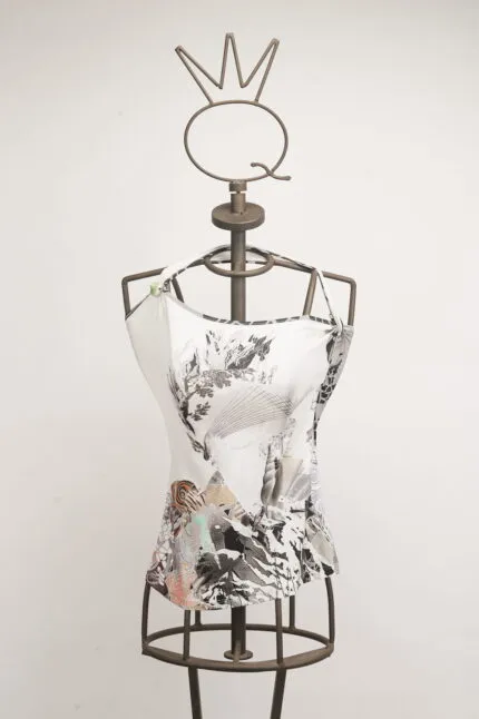 Manichino con top bianco decorato da un design artistico in bianco e nero, esposto su uno sfondo neutro. Il top presenta dettagli grafici colorati e un'originale scollatura asimmetrica, ideale per la moda contemporanea.