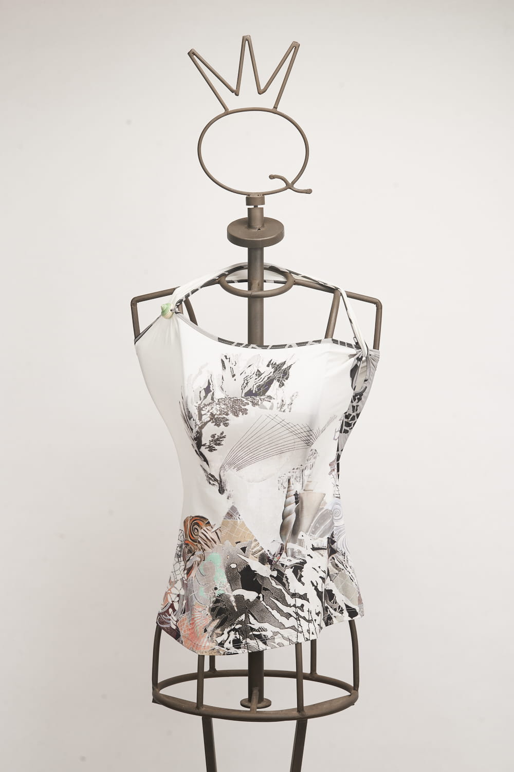 13SSNB624_ 1 Manichino con top bianco decorato da un design artistico in bianco e nero, esposto su uno sfondo neutro. Il top presenta dettagli grafici colorati e un'originale scollatura asimmetrica, ideale per la moda contemporanea.