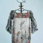 Abito estivo con maniche a sbuffo, caratterizzato da un design multicolore e fantasie floreali, esposto su un manichino su sfondo azzurro.