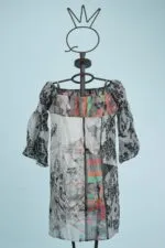 Abito leggero e colorato su manichino, caratterizzato da un design a spalle scoperte e maniche a sbuffo, con motivi astratti in tonalità di nero, bianco e colori vivaci su sfondo azzurro.