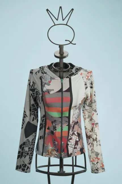 Giacca con cappuccio a maniche lunghe, caratterizzata da un design astratto e colori vivaci, esposta su un manichino con base metallica. Sfondo azzurro per un contrasto accattivante.