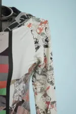 Dettaglio di un abbigliamento femminile con un design astratto e colorato, caratterizzato da una combinazione di forme geometriche e texture, appeso a un supporto su sfondo azzurro.