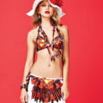 Modella in costume da bagno colorato con accessori coordinati, cappello bianco con fiore rosso e sfondo rosso. Ideale per collezioni estive e moda balneare.