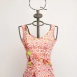 Top à manches courtes pour femme avec motif floral rouge et détails verts, présenté sur un mannequin à support métallique. Design moderne et frais, idéal pour la saison estivale. 