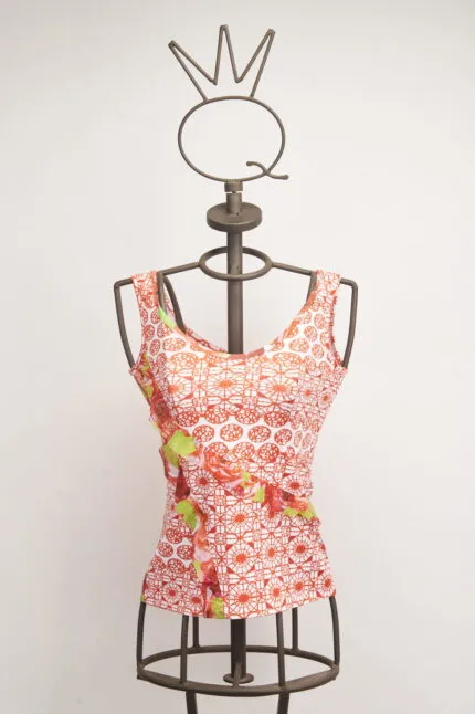 Top donna a maniche corte con motivo floreale rosso e dettagli in verde, esposto su un manichino con supporto metallico. Design moderno e fresco, ideale per la stagione estiva.