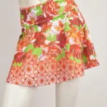 Jupe courte avec des fleurs rouges et vertes sur un mannequin, idéale pour la saison estivale, avec un design vif et frais.