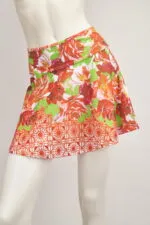 Jupe courte avec des fleurs rouges et vertes sur un mannequin, idéale pour la saison estivale, avec un design vif et frais.