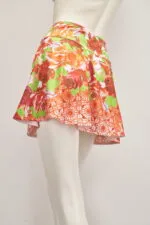 Jupe courte à l'imprimé floral vibrant dans les tons orange et vert, idéale pour la mode et les loisirs d'été. Montrée sur un mannequin, elle met en valeur sa légèreté et son design évasé.