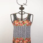 Short-sleeved summer top with floral and geometric pattern, presented on a metal dummy. Lively design with red flowers and black and white details, ideal for casual and cool outfits. 
