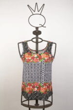 Short-sleeved summer top with floral and geometric pattern, presented on a metal dummy. Lively design with red flowers and black and white details, ideal for casual and cool outfits.
