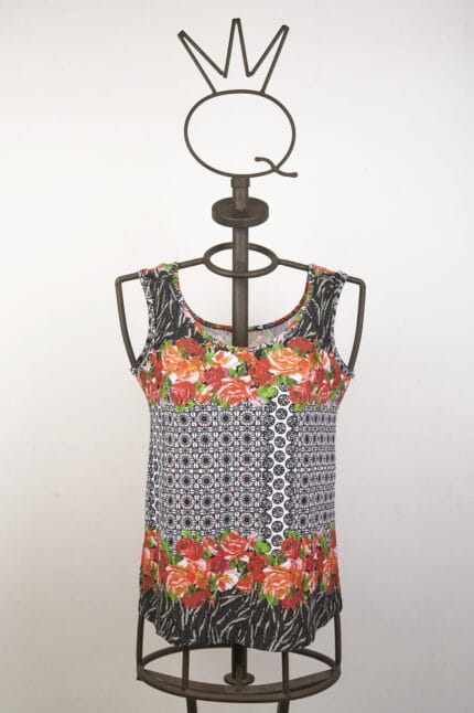 Top estivo a maniche corte con motivo floreale e geometrico, presentato su un manichino in metallo. Design vivace con fiori rossi e dettagli in bianco e nero, ideale per outfit casual e freschi.