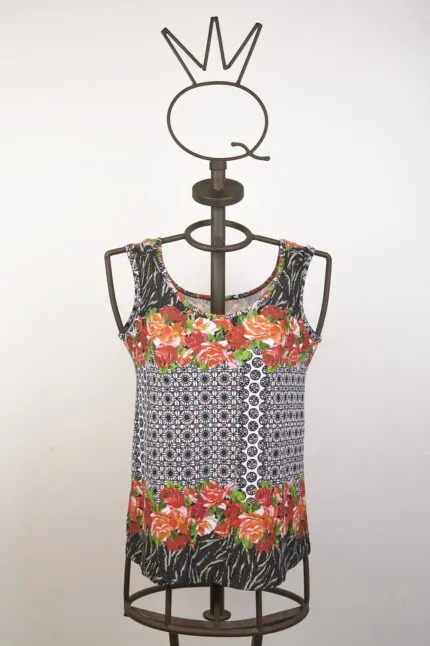 Top estivo a maniche corte con motivo floreale e geometrico, presentato su un manichino in metallo. Design vivace con fiori rossi e dettagli in bianco e nero, ideale per outfit casual e freschi.