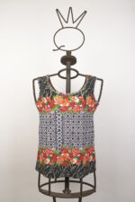 Top estivo senza maniche con motivo floreale in rosso e nero, esposto su un manichino artistico. Design elegante e vivace, ideale per la stagione calda e per abbinamenti casual.