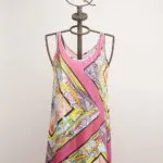 Abito estivo colorato con motivi floreali e geometrie, appeso a un manichino con una corona. Perfetto per occasioni informali e giornate soleggiate.