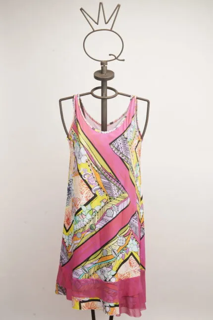 Abito estivo colorato con motivi floreali e geometrie, appeso a un manichino con una corona. Perfetto per occasioni informali e giornate soleggiate.