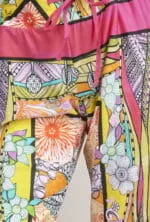 Pantaloni colorati con motivi floreali e geometrici, caratterizzati da una cintura elastica e un laccio rosa, ideali per un look estivo vivace e alla moda.