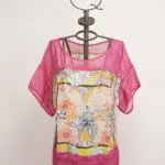 Top estivo colorato con maniche corte, caratterizzato da un motivo floreale vivace e dettagli in rete rosa. Esposto su un manichino decorativo con una corona. Ideale per outfit estivi e occasioni casual.