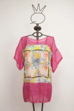 Top estivo colorato con maniche a sbuffo, caratterizzato da un design floreale vivace e trasparente, esposto su un manichino artistico. Perfetto per la stagione calda e per un look casual e alla moda.