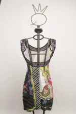 Abito colorato con motivi grafici appeso a una gruccia, presentato su un manichino con una corona stilizzata. Design moderno e vivace perfetto per occasioni estive.