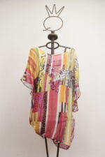 Blusa estiva colorata con motivi floreali e righe, appesa a una gruccia metallica. Adatta per look casual e freschi.