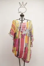 Blusa estiva colorata con motivi floreali e righe, appesa a una gruccia metallica. Adatta per look casual e freschi.