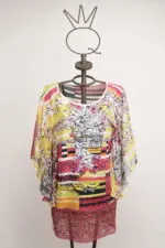 Maglietta colorata a maniche larghe esposta su un manichino, caratterizzata da motivi floreali e strisce vivaci, ideale per un look estivo e casual.