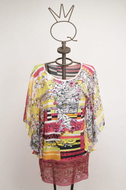 Maglietta colorata a maniche larghe esposta su un manichino, caratterizzata da motivi floreali e strisce vivaci, ideale per un look estivo e casual.
