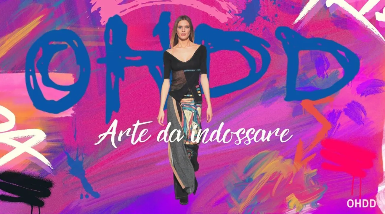 Modella in passerella indossa un abito creativo e colorato, rappresentante il concetto di "arte da indossare", con un fondo vivace e artistico. Logo OHDD presente nell'angolo destro.